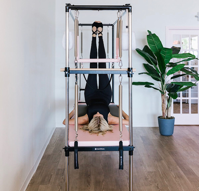 woman in pebbles pilates jumpsuit on cadillac reformer